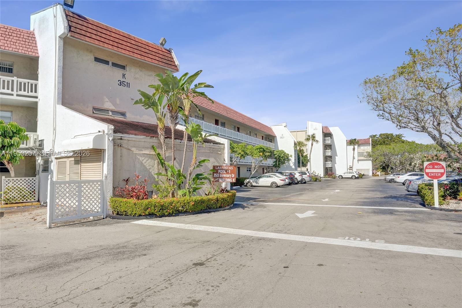 An exterior view of a multi-story apartment building with a parking lot and landscaping — 3511 E Inverrary Dr # 107, Lauderhill FL 33319, LAUDERHILL, FL