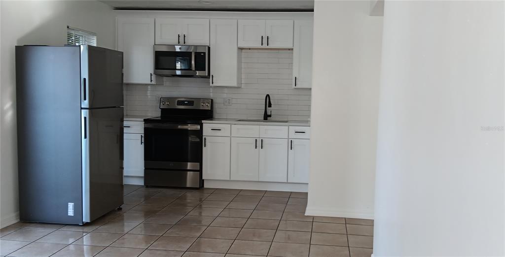 A kitchen features white cabinets, stainless steel appliances, a subway tile backsplash, and tiled flooring — 885 BELTREES STREET UNIT 12, DUNEDIN, FL