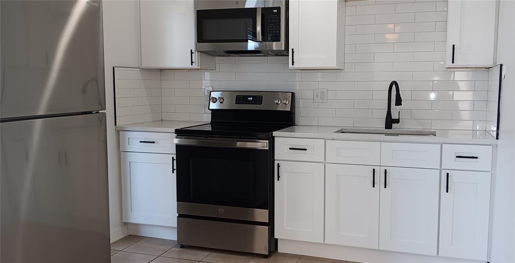 A kitchen with white cabinets, stainless steel appliances, a black faucet, and white subway tile — 885 BELTREES STREET UNIT 12, DUNEDIN, FL