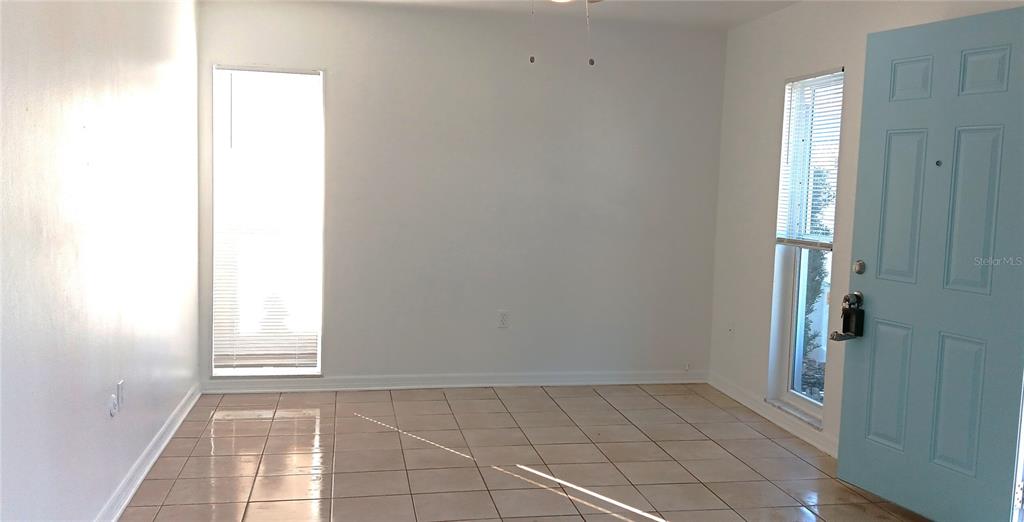 An empty room with tiled floors, white walls, two windows, and a light blue door — 885 BELTREES STREET UNIT 12, DUNEDIN, FL