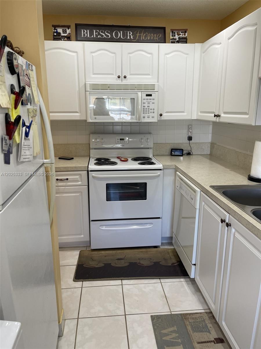 A small kitchen features white cabinets, white appliances, and light-colored tile flooring — 1640 NW 19th Ter # 103, Delray Beach FL 33445, DELRAY BEACH, FL