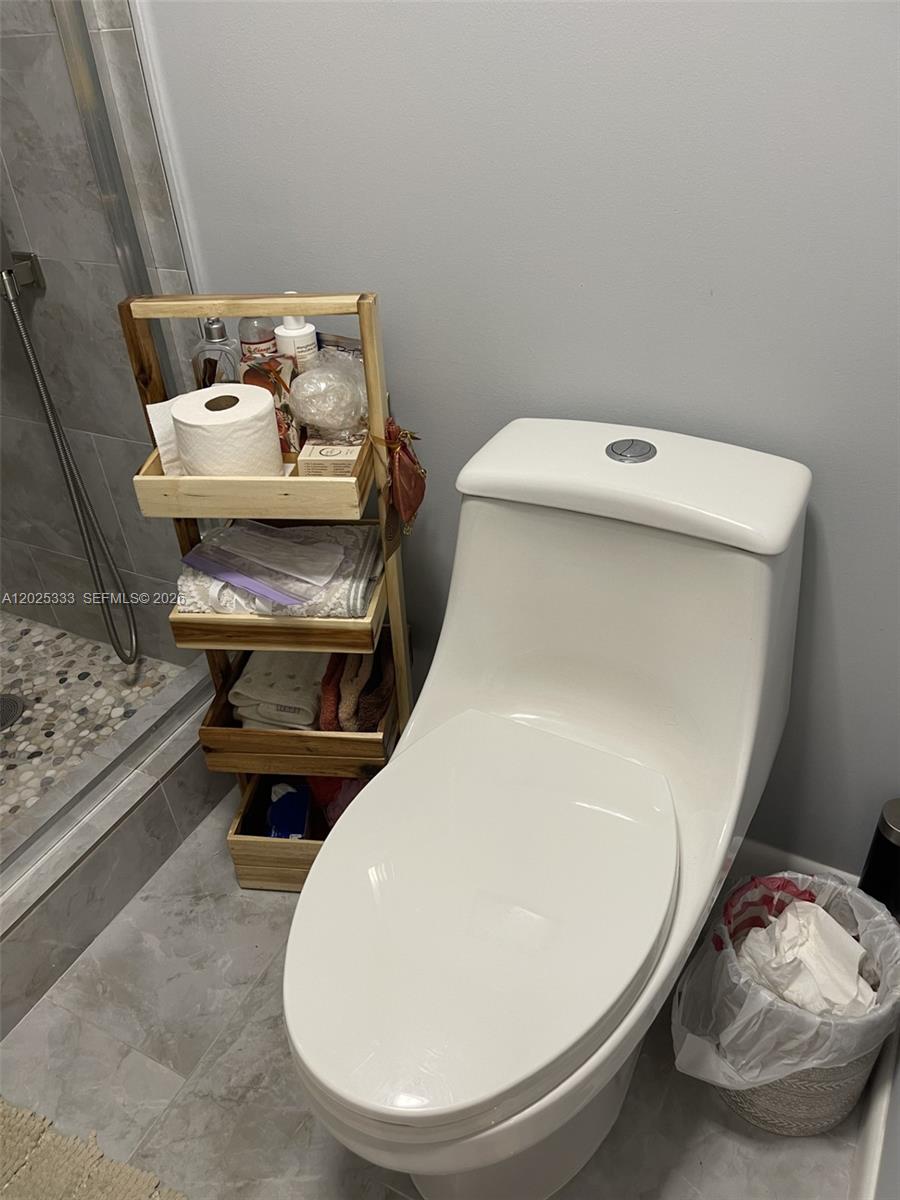 A bathroom features a white toilet, a wooden storage rack, and a glass-enclosed shower — 1640 NW 19th Ter # 103, Delray Beach FL 33445, DELRAY BEACH, FL