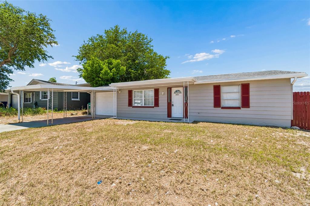 A single-story house with a carport, tan siding, and red shutters under a blue sky — 3521 OAKHURST DRIVE, HOLIDAY, FL
