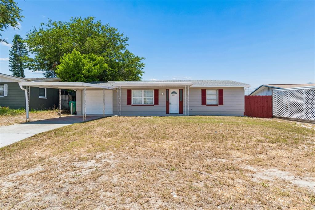A single-story house with a carport, light gray siding, and red shutters under a blue sky — 3521 OAKHURST DRIVE, HOLIDAY, FL