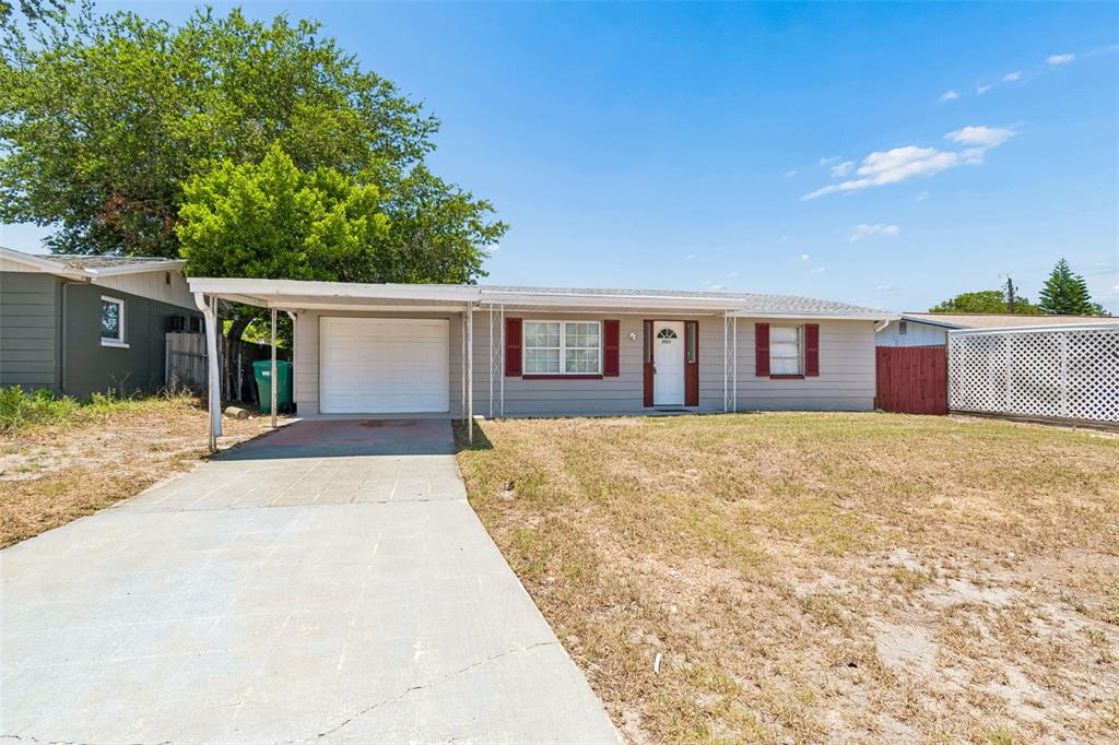 A single-story house with a carport, concrete driveway, and gray siding under a blue sky — 3521 OAKHURST DRIVE, HOLIDAY, FL
