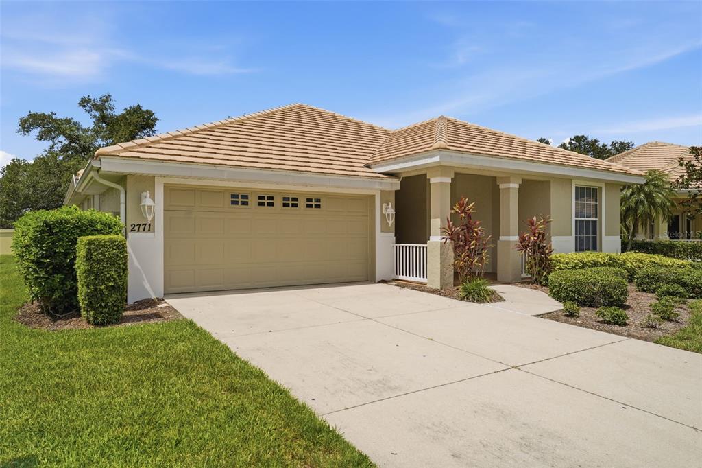 A single-story house with a tan stucco exterior, a tile roof, and a two-car garage — 2771 WHISPERING PINE LANE, NORTH PORT, FL