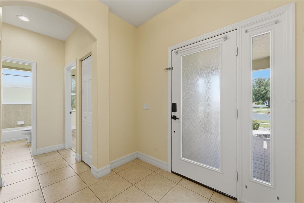 An entryway with light tile flooring, a white front door, and a nearby bathroom door — 2771 WHISPERING PINE LANE, NORTH PORT, FL