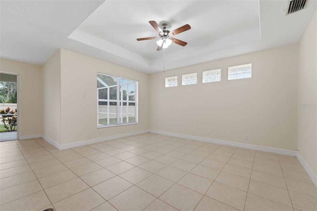 A spacious, empty room with beige tile floors, a tray ceiling, and a ceiling fan — 2771 WHISPERING PINE LANE, NORTH PORT, FL