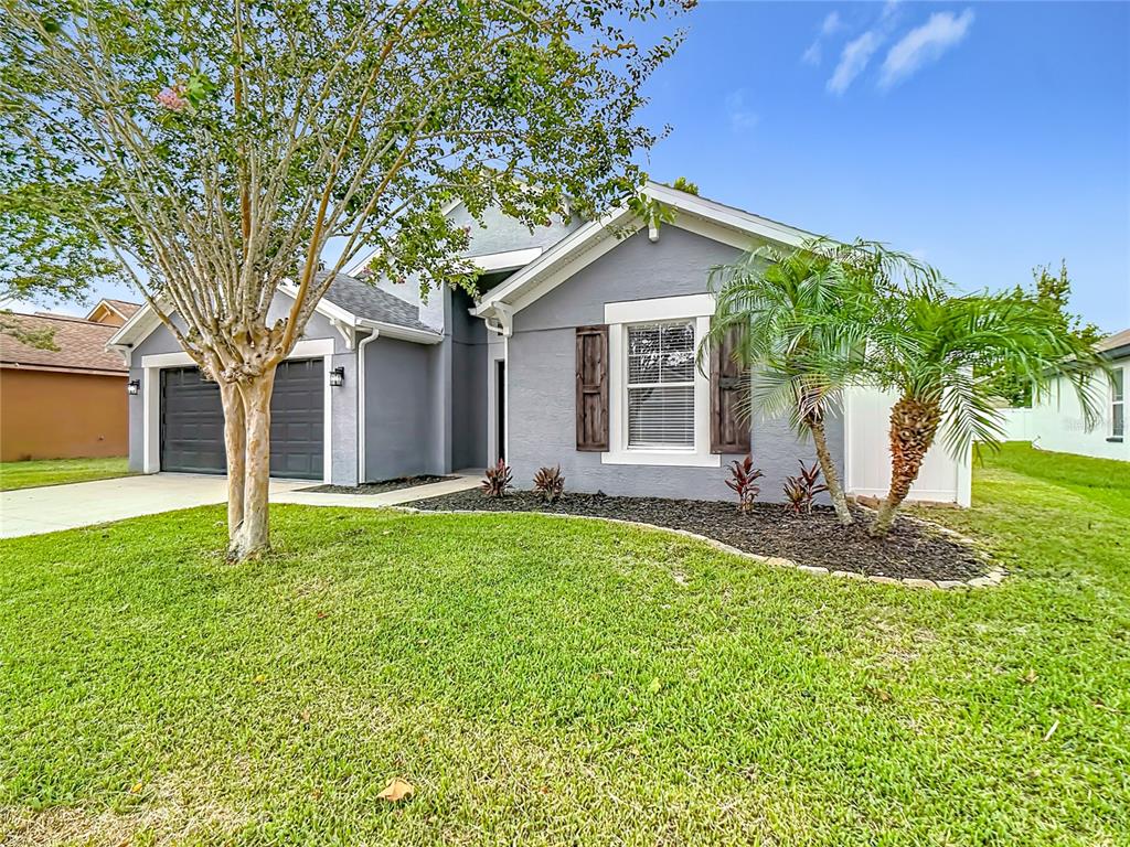 A gray single-story house with a two-car garage, a front lawn, and a palm tree — 8278 PEAK AVENUE, LAKELAND, FL