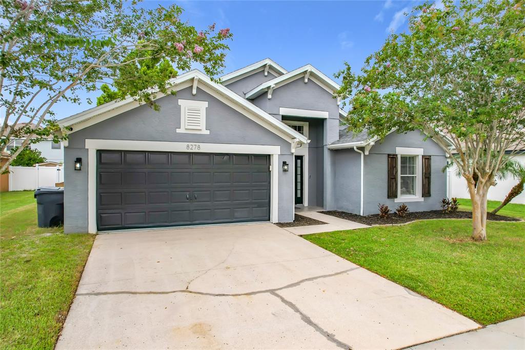 A gray single-story house with a two-car garage and a front lawn with trees — 8278 PEAK AVENUE, LAKELAND, FL