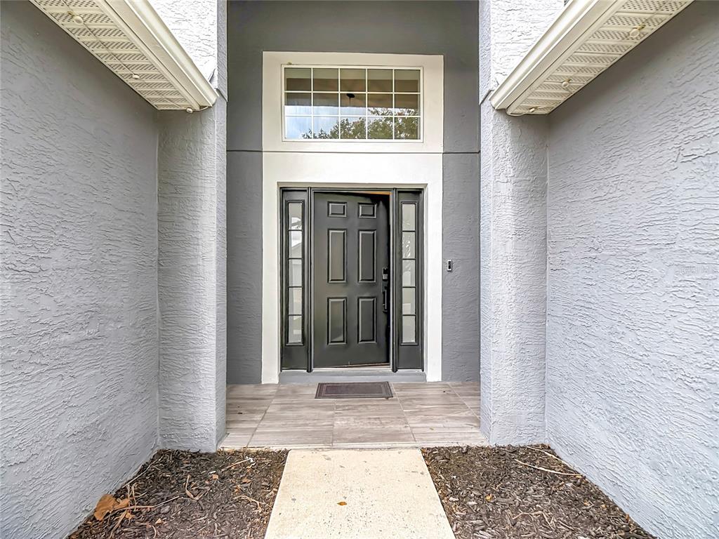 A gray front door with sidelights and a transom window sits under a covered entryway — 8278 PEAK AVENUE, LAKELAND, FL