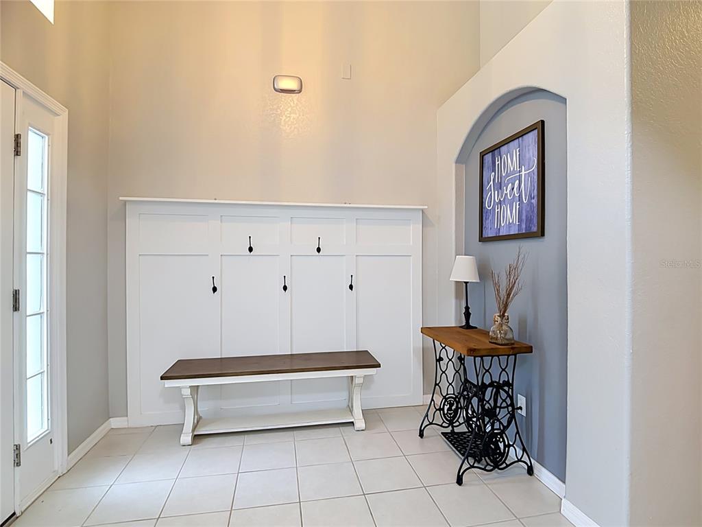 An entryway features a white mudroom bench, a vintage sewing machine table, and wall decor — 8278 PEAK AVENUE, LAKELAND, FL