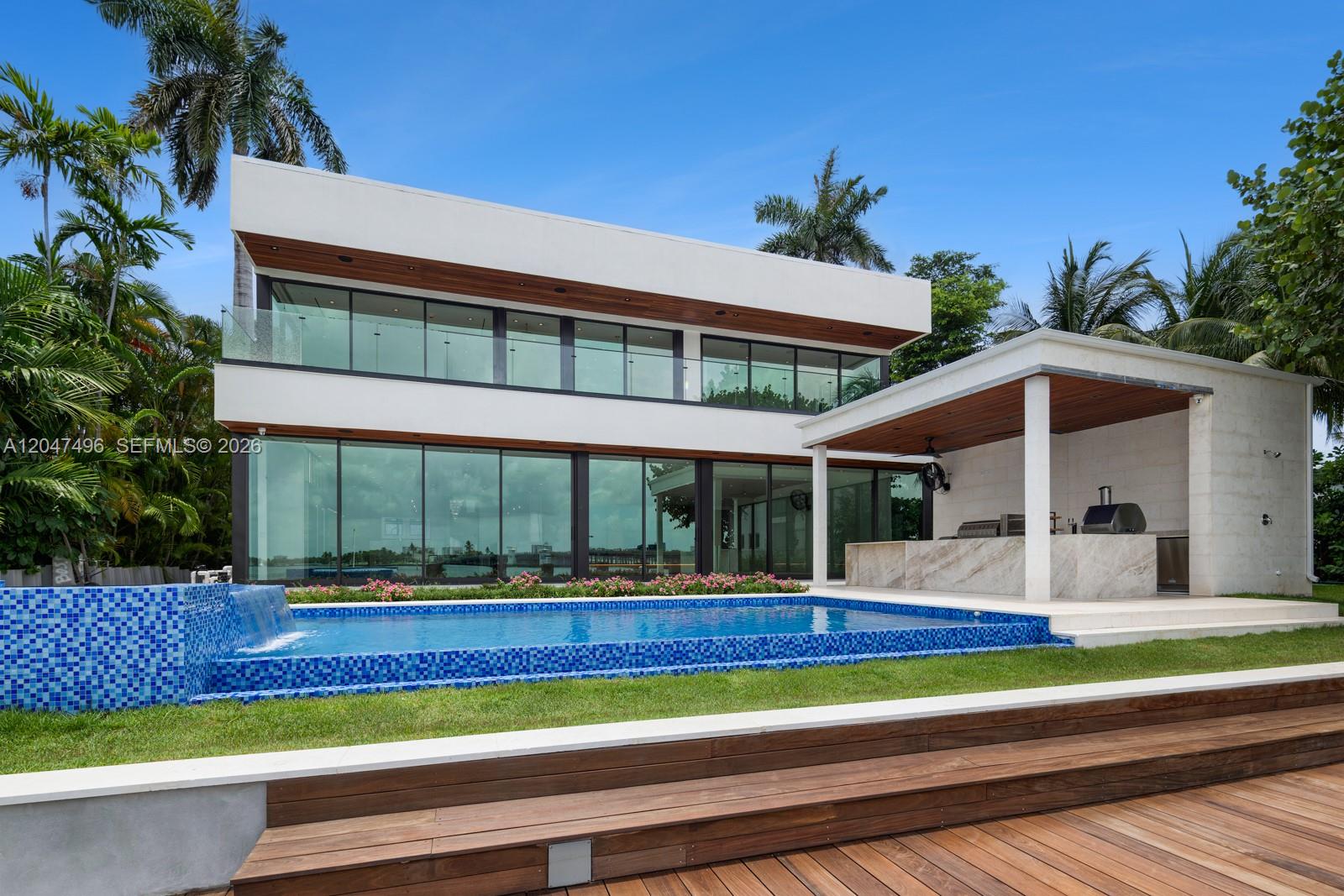 A modern two-story house features a glass facade, a swimming pool, and an outdoor kitchen — 9720 W Broadview Dr, Bay Harbor Islands FL 33154, BAY HARBOR ISLANDS, FL