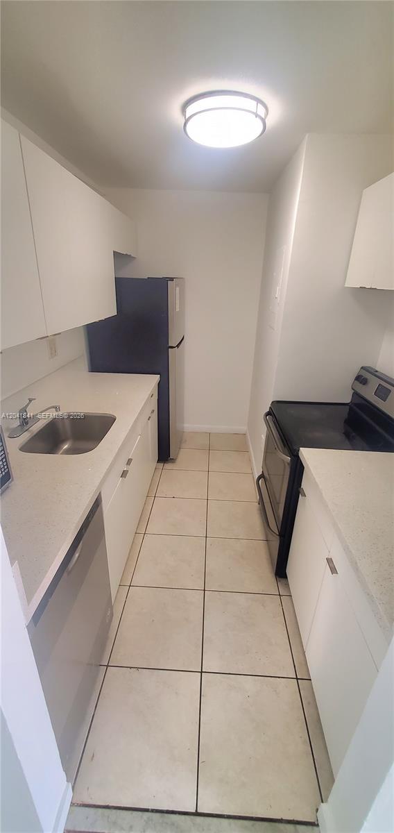 A narrow galley kitchen features white cabinets, light countertops, stainless steel appliances, and tile flooring — 7405 SW 152nd Ave # 3, Miami FL 33193, MIAMI, FL