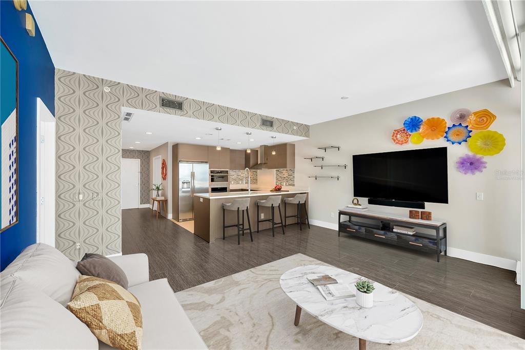 A modern open-concept living room and kitchen featuring gray wood-look flooring and a patterned accent wall — 145 2ND AVENUE S UNIT 521, ST PETERSBURG, FL