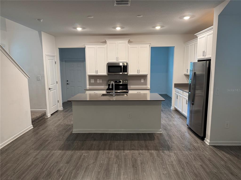A kitchen with white cabinets, stainless steel appliances, a center island, and wood-look flooring — 1652 CROSS PRAIRIE PARKWAY, KISSIMMEE, FL