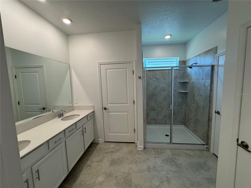 A bathroom features a double vanity, a walk-in shower with tiled walls, and tile flooring — 1652 CROSS PRAIRIE PARKWAY, KISSIMMEE, FL