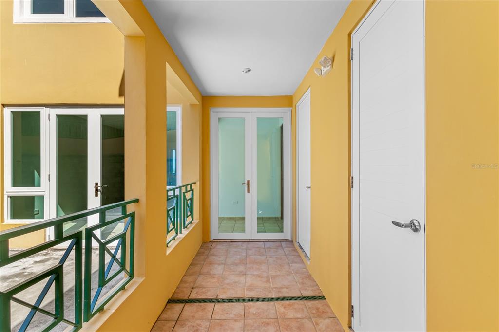 An outdoor hallway with yellow walls, tiled flooring, and white doors — 10 H UNIT 201, RIO GRANDE, PR
