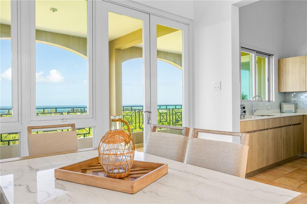 A dining area with a marble table, wicker centerpiece, and views of the ocean outside — 10 H UNIT 201, RIO GRANDE, PR