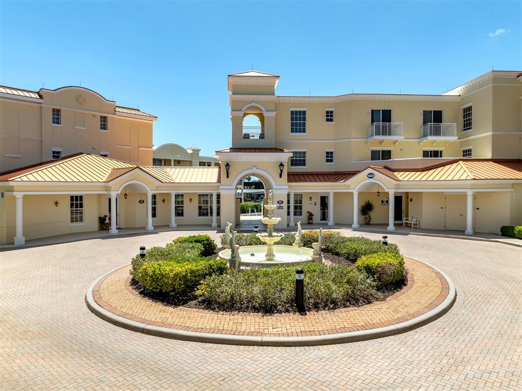 A circular driveway with a central fountain leads to the entrance of a multi-story building — 14021 BELLAGIO WAY UNIT 404, OSPREY, FL