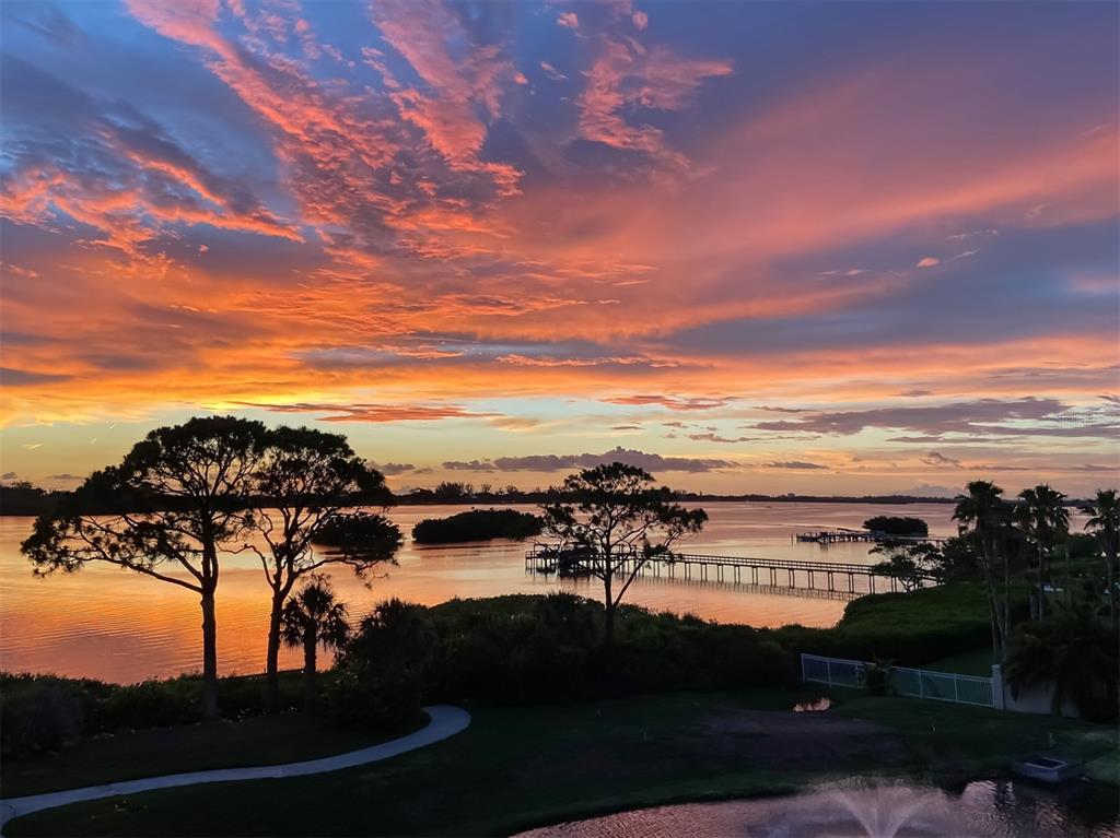 A vibrant sunset view over a calm bay with a long wooden pier and trees — 14021 BELLAGIO WAY UNIT 404, OSPREY, FL