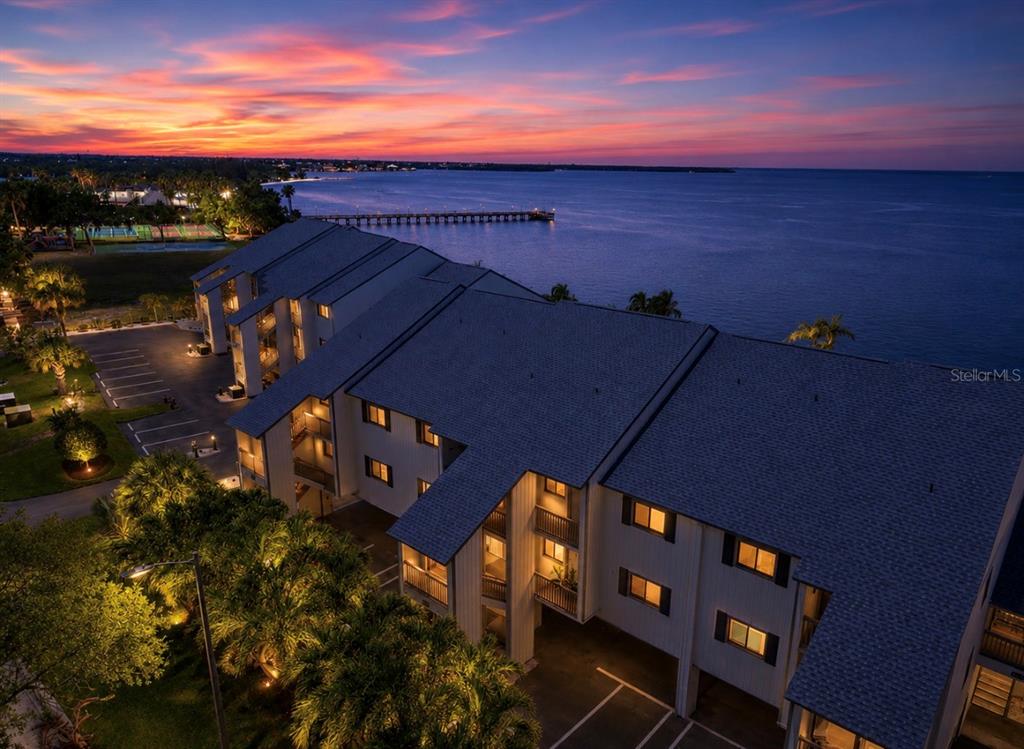 An aerial view shows a multi-story apartment building at sunset next to a pier — 810 BAHIA DEL SOL DRIVE UNIT 16, RUSKIN, FL