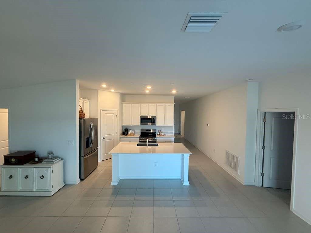 A modern kitchen features white cabinetry, a central island with a sink, and stainless appliances — 2359 POCKY WAY, KISSIMMEE, FL