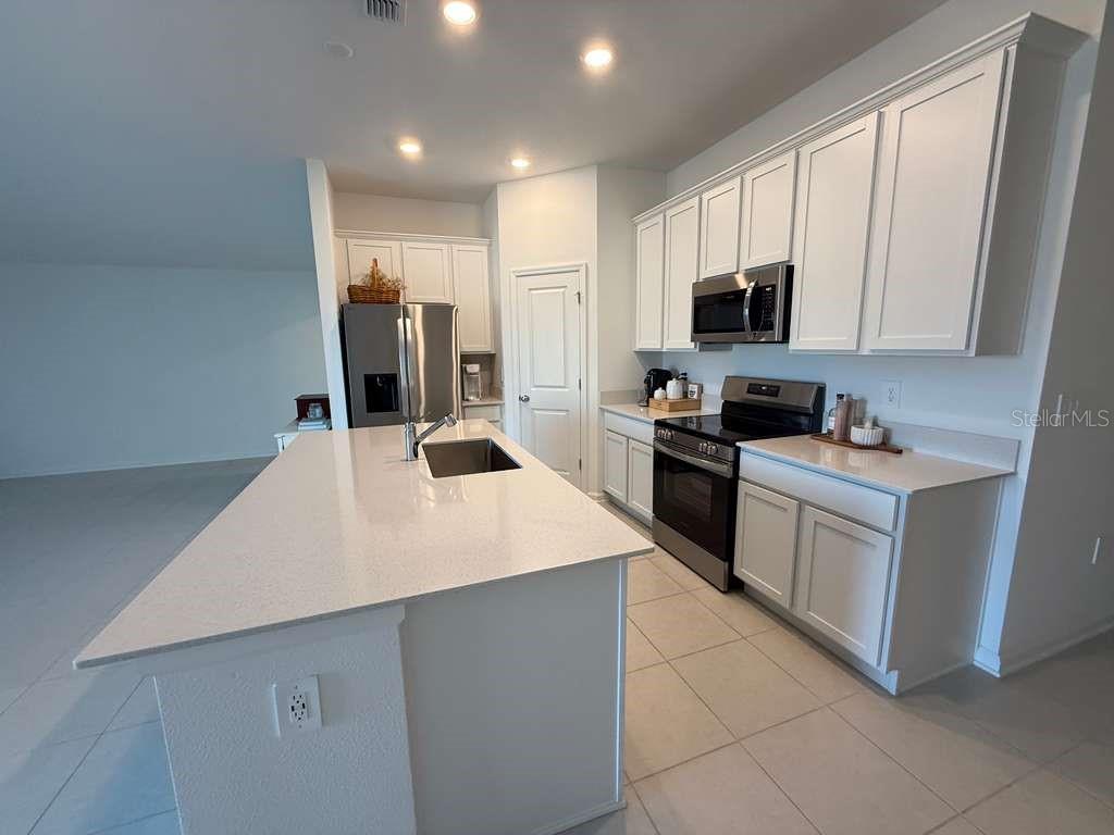 A modern kitchen features white cabinets, stainless steel appliances, and a large quartz-topped island — 2359 POCKY WAY, KISSIMMEE, FL