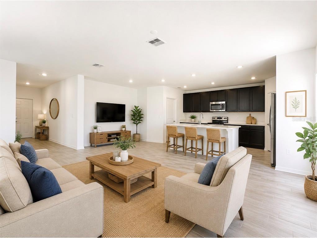 An open-concept living room and kitchen featuring light wood floors and dark cabinetry — 924 SERCHIO STREET, HAINES CITY, FL