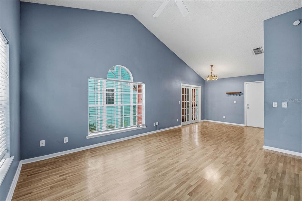 A living room with blue walls, vaulted ceilings, light wood flooring, and a large arched window — 3002 W CLEVELAND STREET UNIT A8, TAMPA, FL