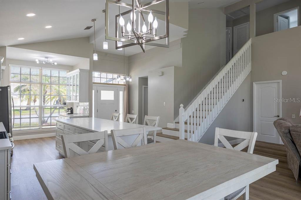 A bright kitchen and dining area features a large island, white cabinetry, and a staircase — 3432 IDLEGROVE COURT, ORLANDO, FL