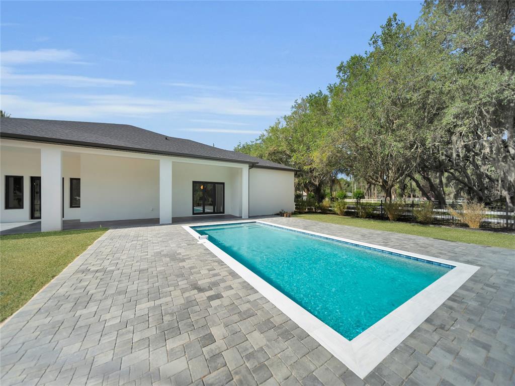 A rectangular swimming pool sits on a paved patio beside a white house with columns — 11241 OSWALT ROAD, CLERMONT, FL