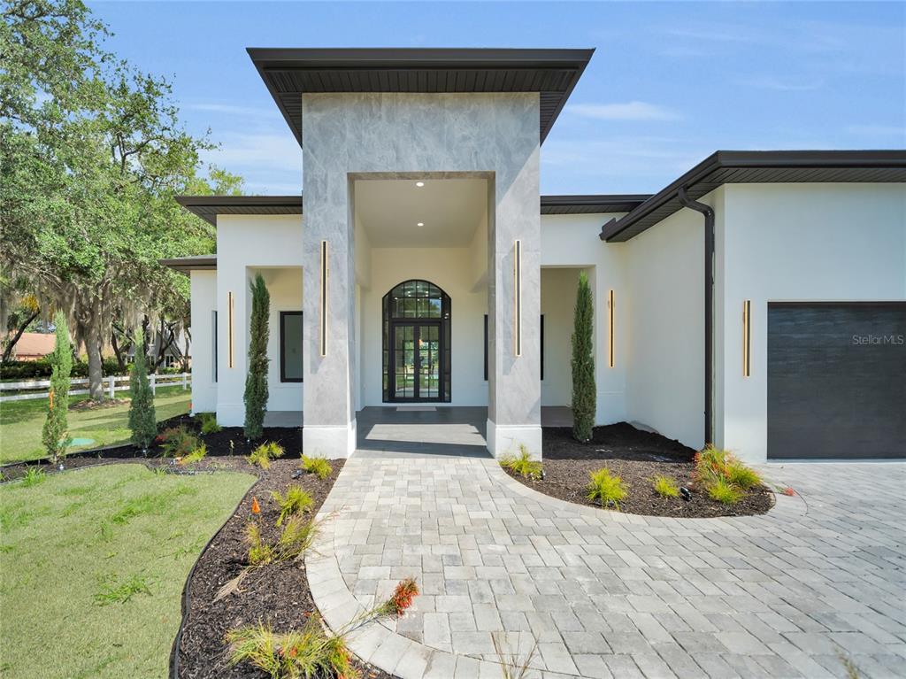 A modern house exterior features a stone-clad entryway, a paved walkway, and a dark garage — 11241 OSWALT ROAD, CLERMONT, FL