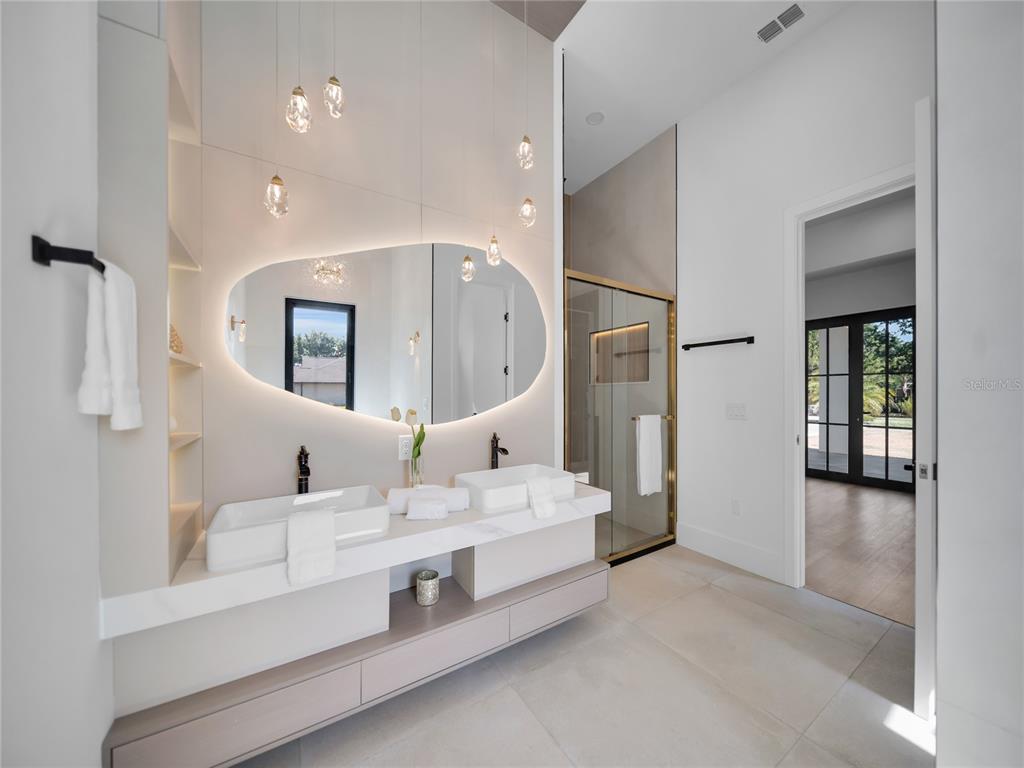 A modern bathroom features a floating double vanity, an organic-shaped backlit mirror, and glass shower — 11241 OSWALT ROAD, CLERMONT, FL