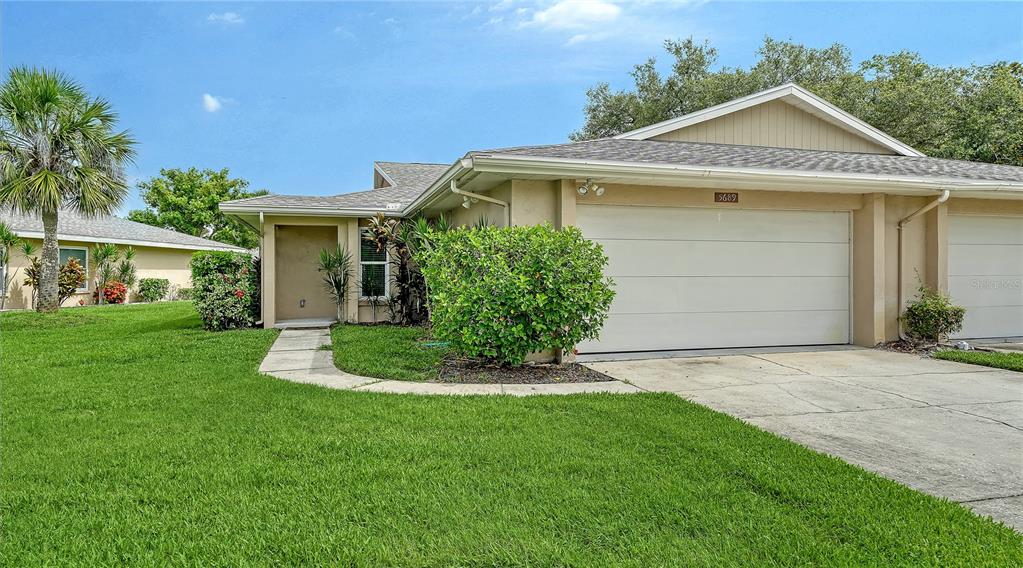 A single-story duplex with a tan exterior, a two-car garage, and a front lawn — 5689 EVERGREEN DRIVE UNIT 18, SARASOTA, FL