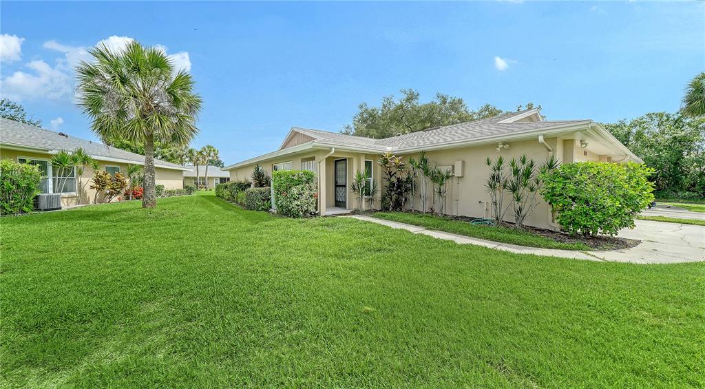A single-story tan house with a palm tree and a green lawn in the foreground — 5689 EVERGREEN DRIVE UNIT 18, SARASOTA, FL