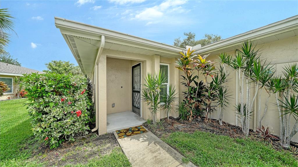 The exterior of a house features a covered entryway, a concrete walkway, and landscaped bushes — 5689 EVERGREEN DRIVE UNIT 18, SARASOTA, FL