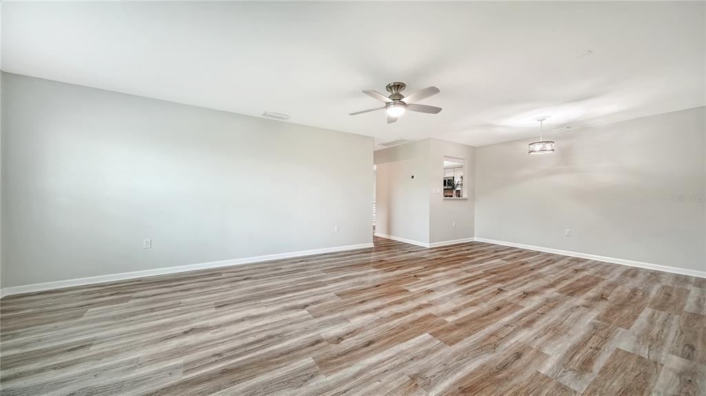 A spacious room with light gray walls, wood-look flooring, a ceiling fan, and a light fixture — 5689 EVERGREEN DRIVE UNIT 18, SARASOTA, FL