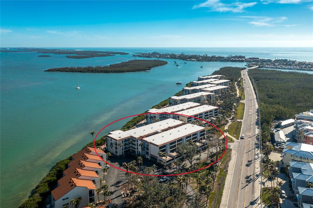 An aerial view shows a multi-story waterfront apartment complex located beside a coastal road — 1501 BEACH ROAD UNIT 210, ENGLEWOOD, FL