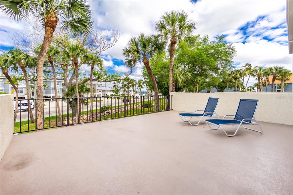 A spacious outdoor balcony features two lounge chairs, a metal railing, and palm trees — 1501 BEACH ROAD UNIT 210, ENGLEWOOD, FL
