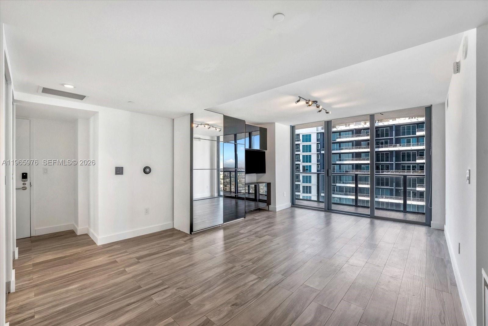 A modern living room features light wood floors, mirrored walls, and floor-to-ceiling windows — 1300 S Miami Ave # 4807, Miami FL 33130, MIAMI, FL