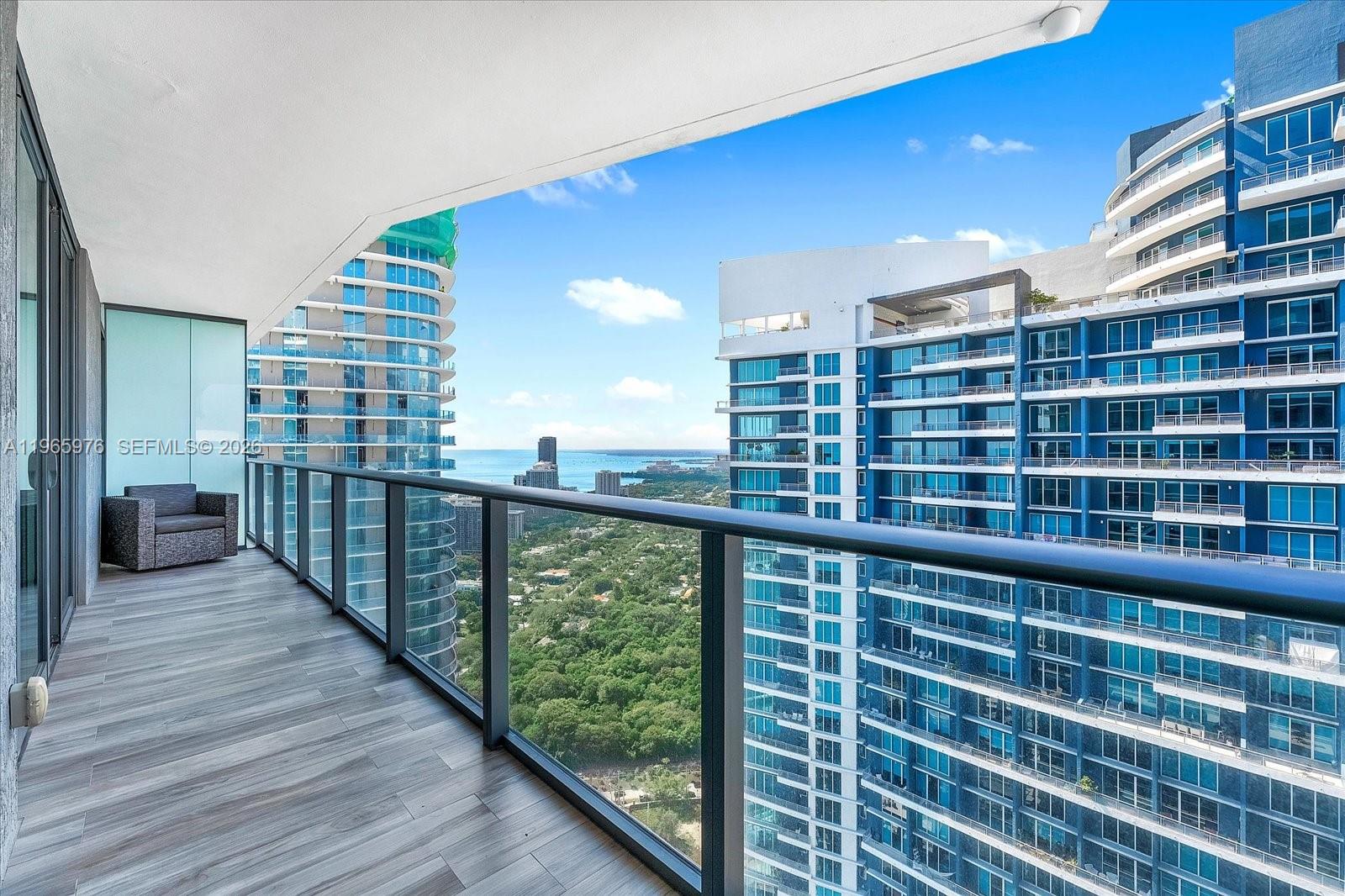 A balcony with wood-look tile flooring overlooks a city skyline and the ocean — 1300 S Miami Ave # 4807, Miami FL 33130, MIAMI, FL
