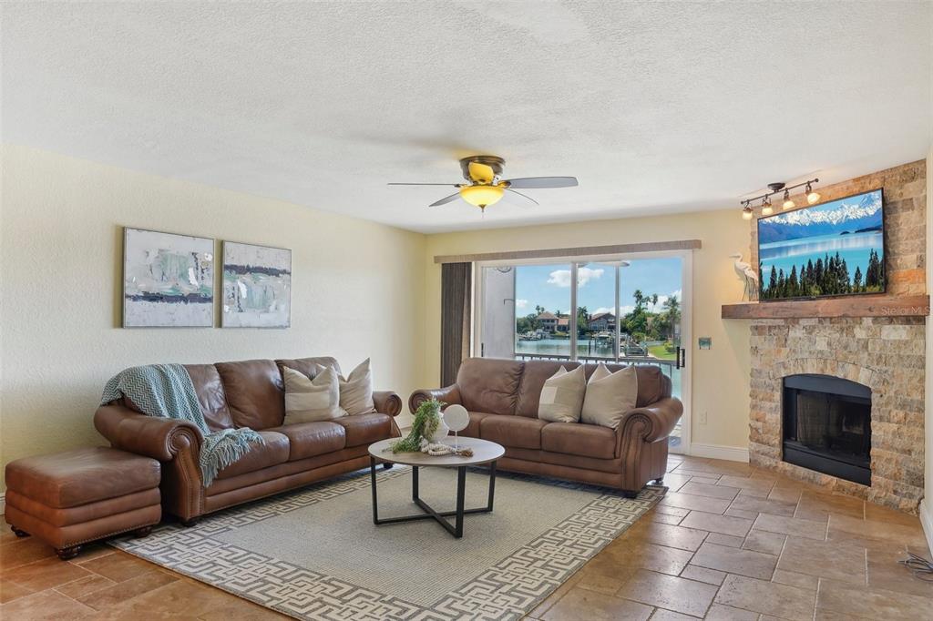 A living room features brown leather sofas, a stone fireplace, and a sliding glass door — 637 PINELLAS BAYWAY UNIT 105, TIERRA VERDE, FL