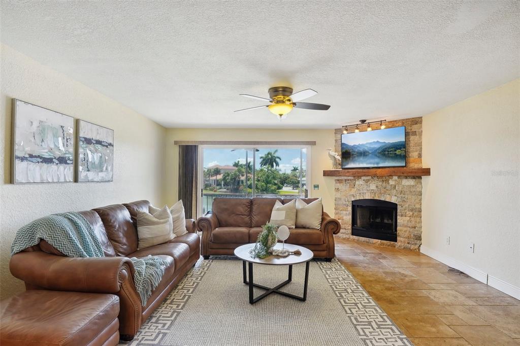 A living room features brown leather sofas, a stone fireplace, and a sliding glass door — 637 PINELLAS BAYWAY UNIT 105, TIERRA VERDE, FL
