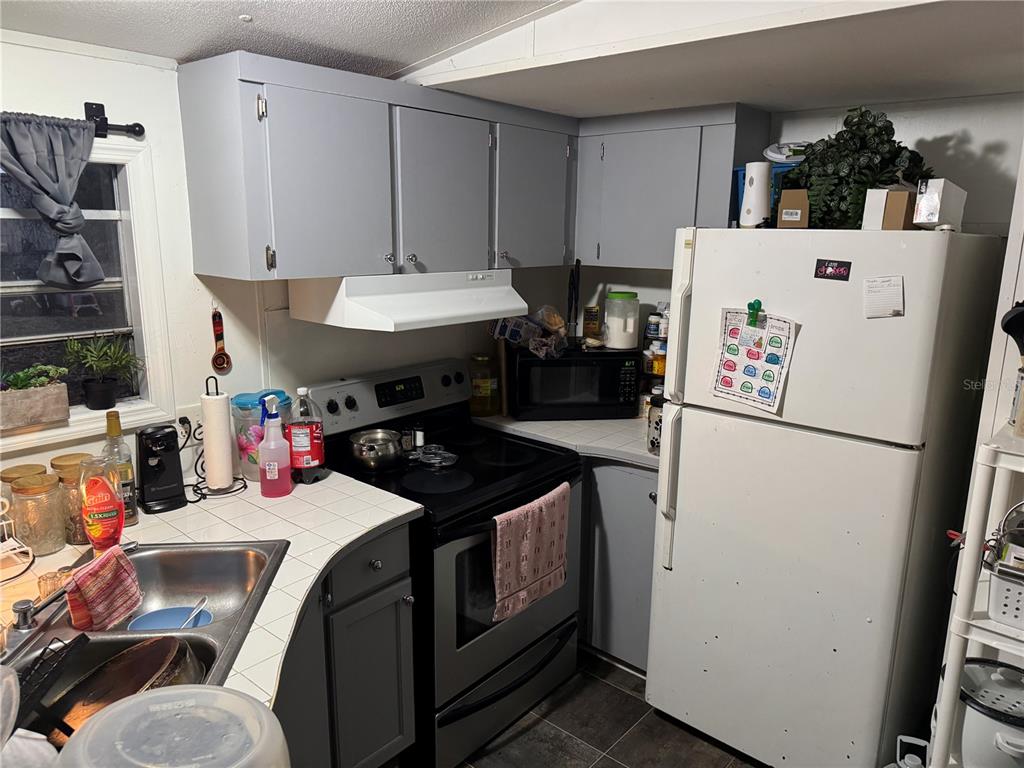 A kitchen features gray cabinets, a white refrigerator, a black stove, and tiled countertops — 18110 SPANGLER AVENUE, BROOKSVILLE, FL