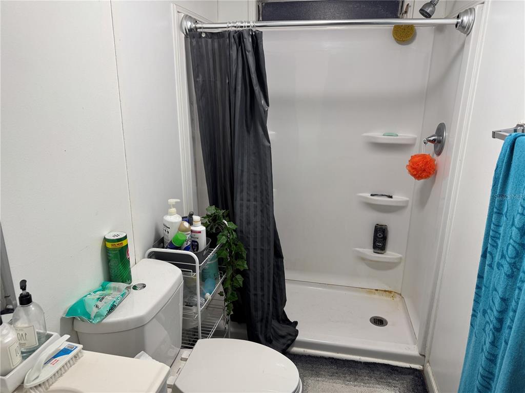 A bathroom features a white toilet, a wire storage rack, and a shower stall — 18110 SPANGLER AVENUE, BROOKSVILLE, FL