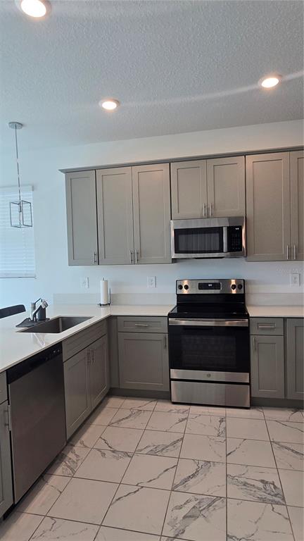 A kitchen features gray cabinets, stainless steel appliances, white countertops, and white marble-patterned floor tiles — 7733 STONE CREEK TRAIL, KISSIMMEE, FL