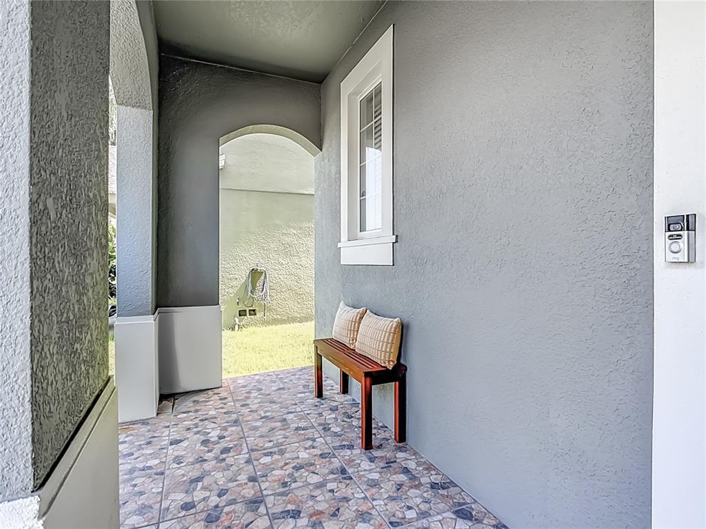 A covered porch features a tiled floor, a wooden bench, and a gray stucco wall — 1553 CATERPILLAR STREET, ST CLOUD, FL