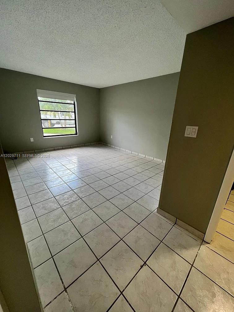 An empty room features light-colored tile flooring, gray walls, and a single window — 1300 SW 122nd Ave # 2, Miami FL 33184, MIAMI, FL