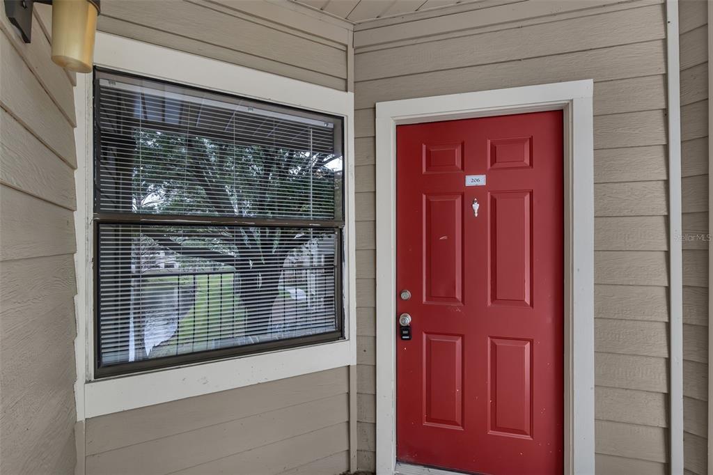 A red front door with the number 206 sits next to a window with blinds — 3016 PARKWAY BOULEVARD UNIT 206, KISSIMMEE, FL